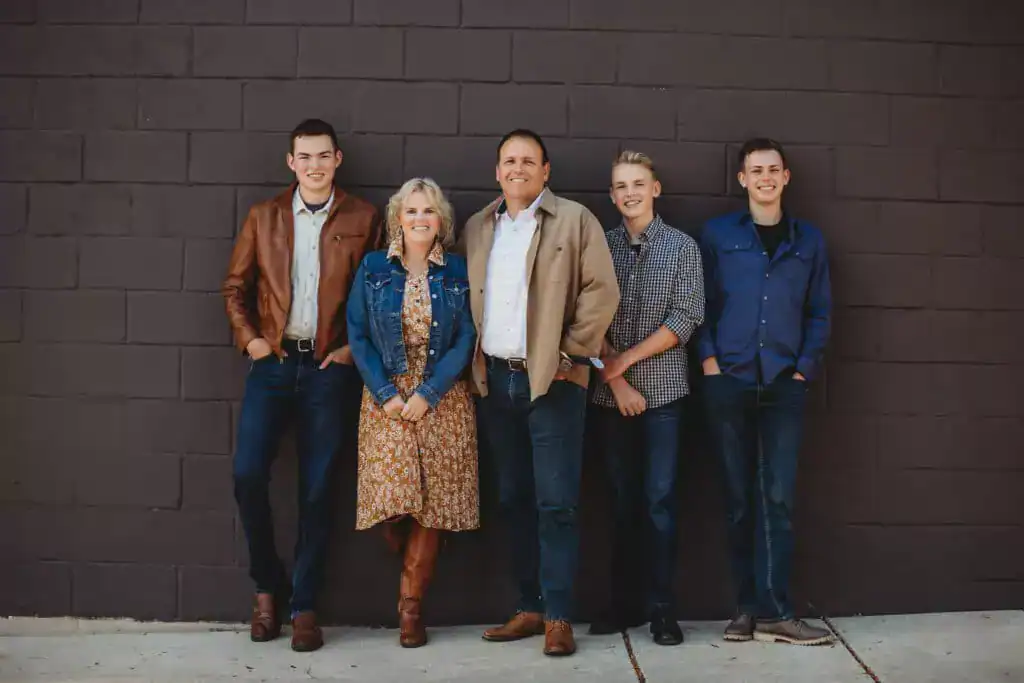 About Us: The owner and his family stand in front of a brick wall. They are wearing casual clothing and all are smiling at the camera.