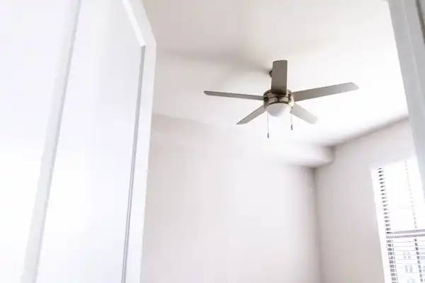 Ceiling fan with four blades and a light fixture in a white room, viewed from a doorway.